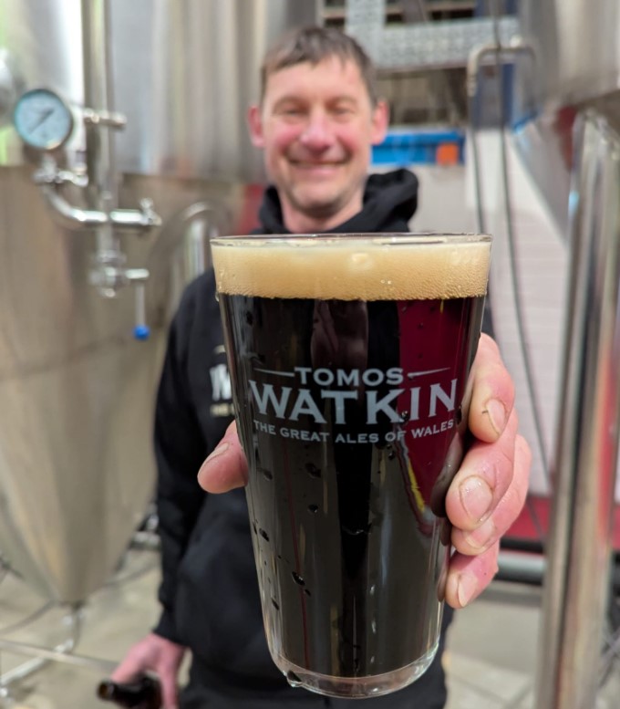 Tomos Watkin holding glass in brewery